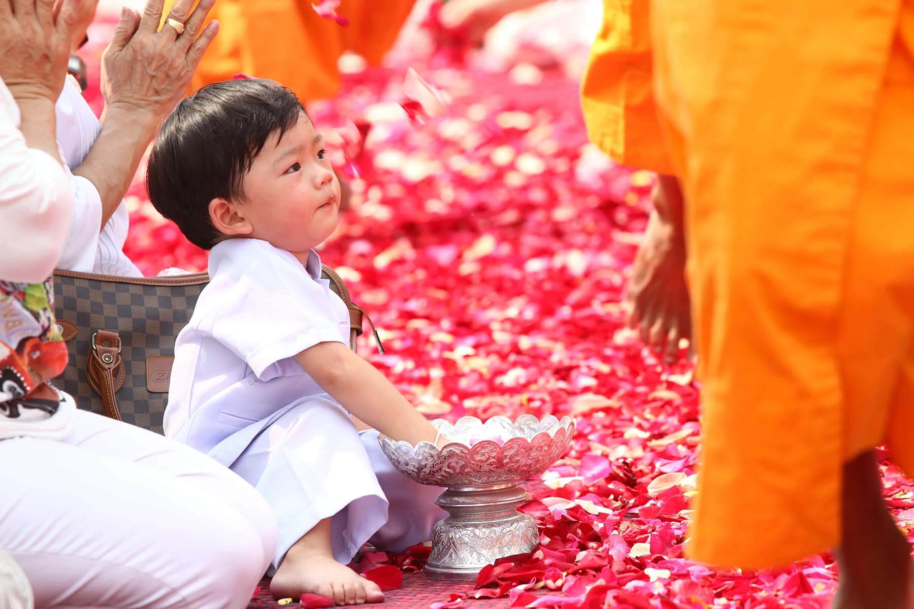 Toddler surrounded by flowers at Buddhist festival.